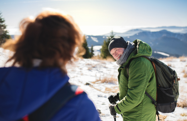 Senior couple hikers with nordic walking poles in snow-covered winter nature, resting.