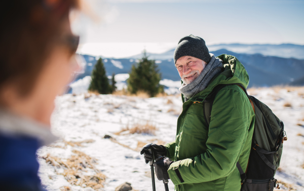 Senior couple hikers with nordic walking poles in snow-covered winter nature, resting.