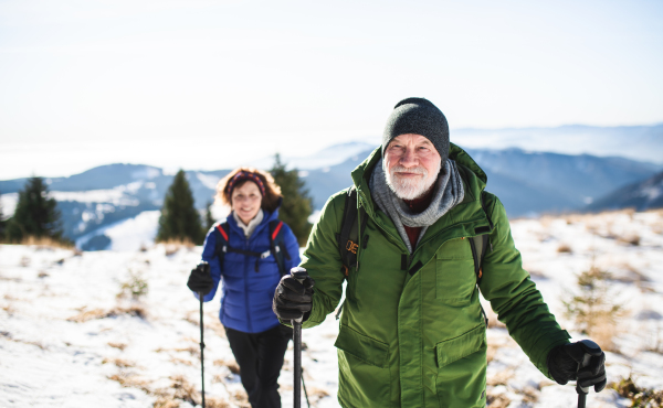 Senior couple with nordic walking poles hiking in snow-covered winter nature, healthy lifestyle concept.