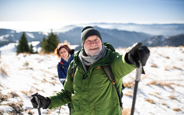 Senior couple hikers with nordic walking poles in snow-covered winter nature, resting.