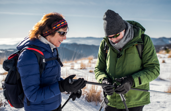 Senior couple hikers with nordic walking poles in snow-covered winter nature, resting.