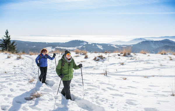 Senior couple with nordic walking poles hiking in snow-covered winter nature, healthy lifestyle concept.