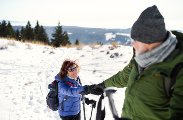 Senior couple with nordic walking poles hiking in snow-covered winter nature, healthy lifestyle concept.