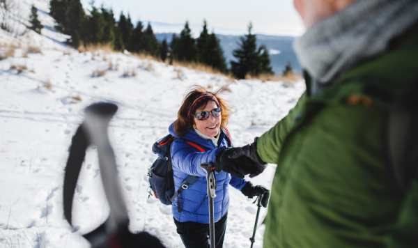 Senior couple with nordic walking poles hiking in snow-covered winter nature, healthy lifestyle concept.