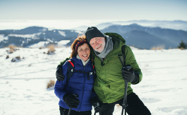 Senior couple hikers with nordic walking poles in snow-covered winter nature, looking at camera.