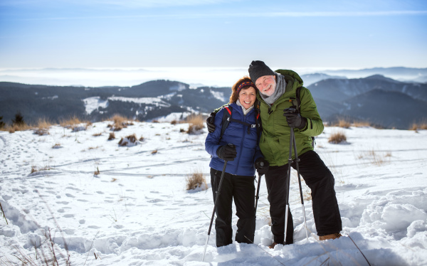 Senior couple hikers with nordic walking poles in snow-covered winter nature, looking at camera.