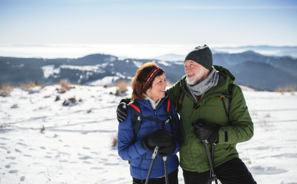 Senior couple hikers with nordic walking poles in snow-covered winter nature, resting.