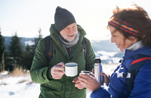 Senior couple hikers resting in snow-covered winter nature, drinking hot tea.