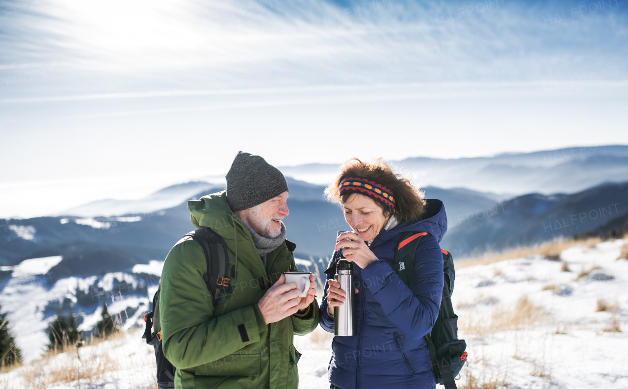 Senior couple hikers resting in snow-covered winter nature, drinking hot tea.