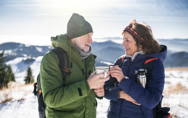 Senior couple hikers resting in snow-covered winter nature, drinking hot tea.