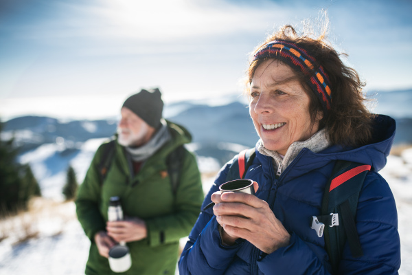 Senior couple hikers resting in snow-covered winter nature, drinking hot tea.