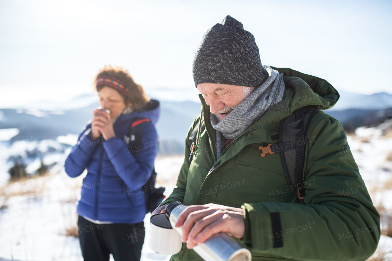 Senior couple hikers resting in snow-covered winter nature, drinking hot tea.