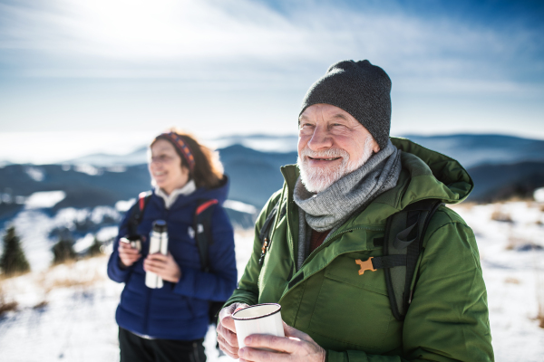 Senior couple hikers resting in snow-covered winter nature, drinking hot tea.