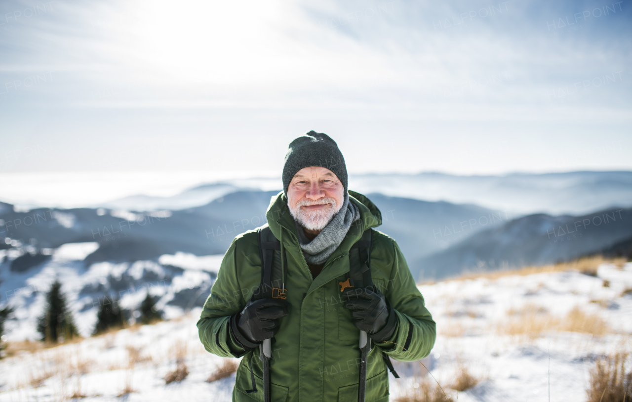 Front view portrait of senior man standing in snow-covered winter nature, looking at camera.