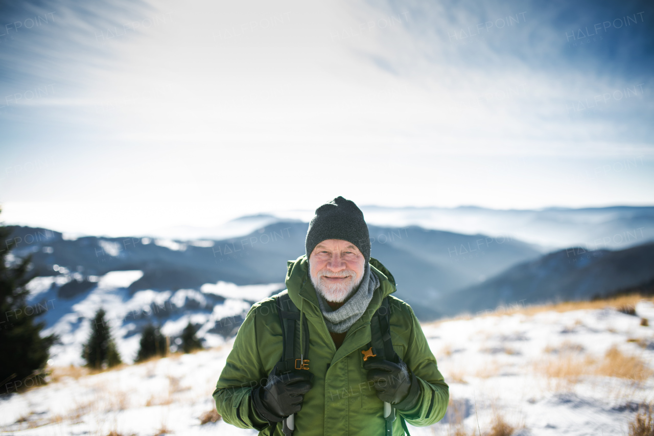 Front view portrait of senior man standing in snow-covered winter nature, looking at camera.