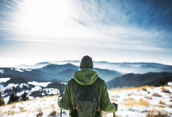 Rear view of senior man hiker in snow-covered winter nature, standing. Copy space.