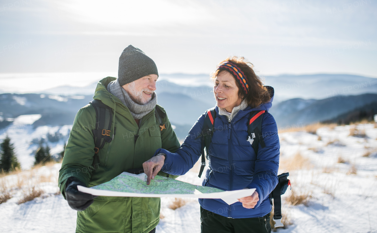 Portrait of senior couple hikers using map in snow-covered winter nature.