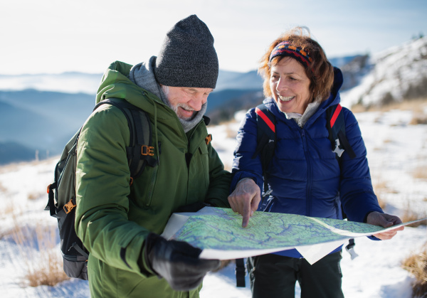 Portrait of senior couple hikers using map in snow-covered winter nature.