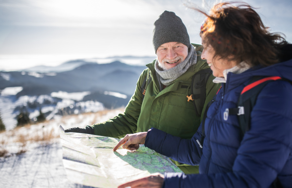 Portrait of senior couple hikers using map in snow-covered winter nature.