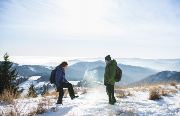 Side view of senior couple hikers standing in snow-covered winter nature, having fun.