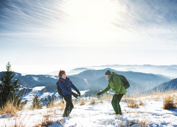 Side view of senior couple hikers standing in snow-covered winter nature, having fun.