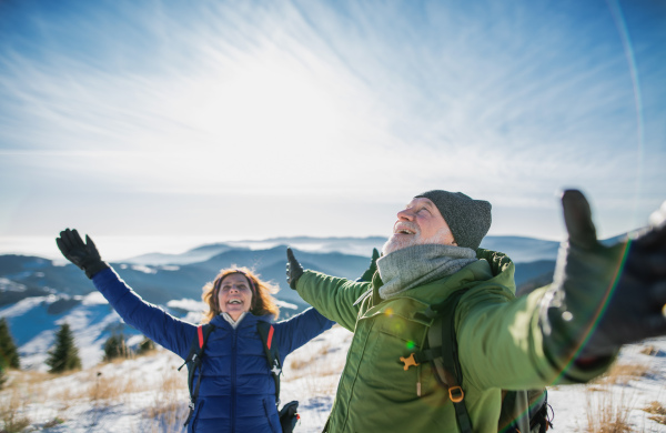 Happy senior couple hikers in snow-covered winter nature, stretching arms.