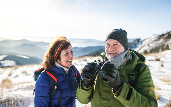 Portrait of senior couple hikers using binoculars in snow-covered winter nature.