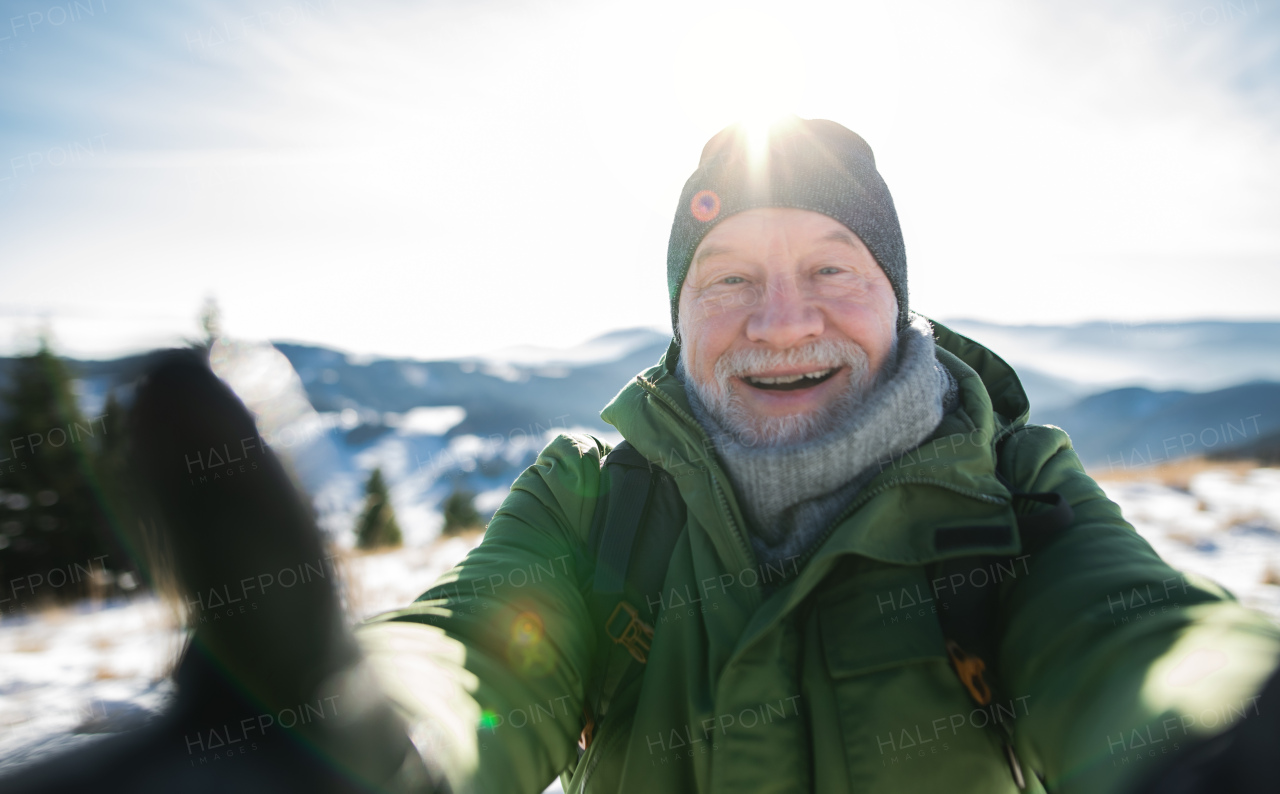 Front view portrait of senior man standing in snow-covered winter nature, looking at camera.