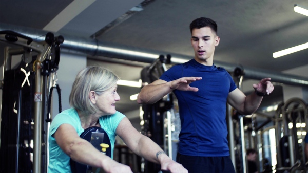 A cheerful female senior with a young trainer doing strength workout exercise in gym.