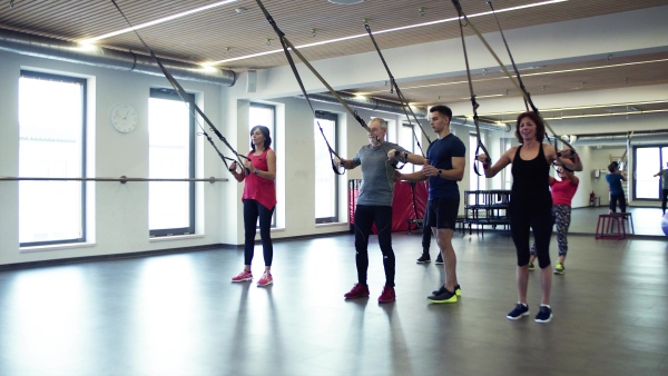 A group of cheerful seniors in gym with a young personal trainer doing exercise with TRX.