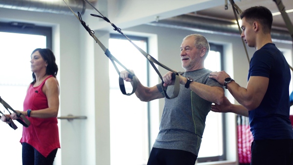 A group of cheerful seniors in gym with a young personal trainer doing exercise with TRX.