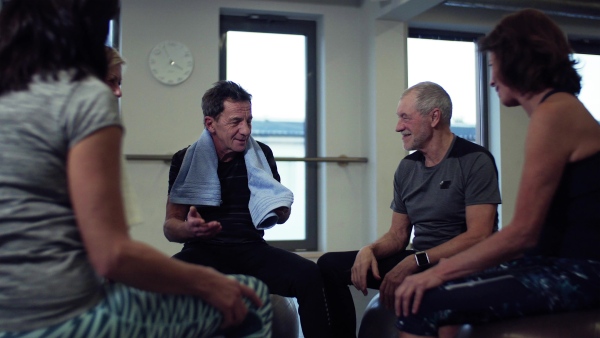 A group of cheerful seniors in gym resting after doing exercise on fit balls, talking.