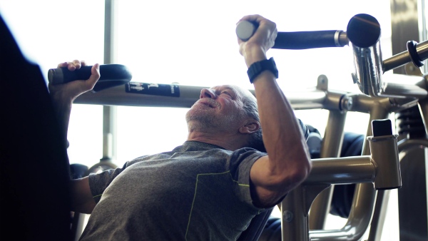 A concentrated senior man doing strength workout exercise in gym.