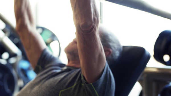 A concentrated senior man doing strength workout exercise in gym.