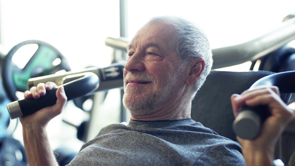 A concentrated senior man doing strength workout exercise in gym.