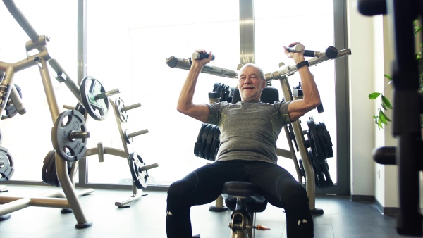 A concentrated senior man doing strength workout exercise in gym.