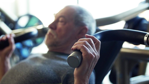 A concentrated senior man doing strength workout exercise in gym. Slow motion.