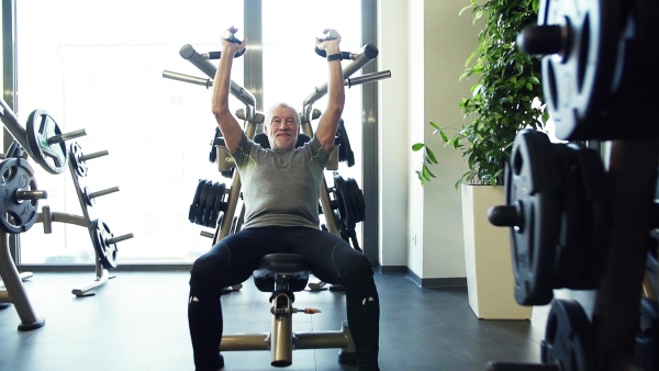 A concentrated senior man doing strength workout exercise in gym. Slow motion.