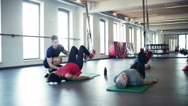 A group of cheerful seniors in gym with a young personal trainer doing exercise with TRX. Slow motion.