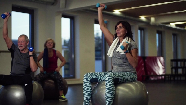 A group of cheerful seniors in gym doing exercise with dumbbells on fit balls. Slow motion.