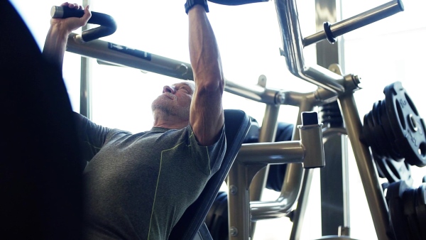 A concentrated senior man doing strength workout exercise in gym. Slow motion.