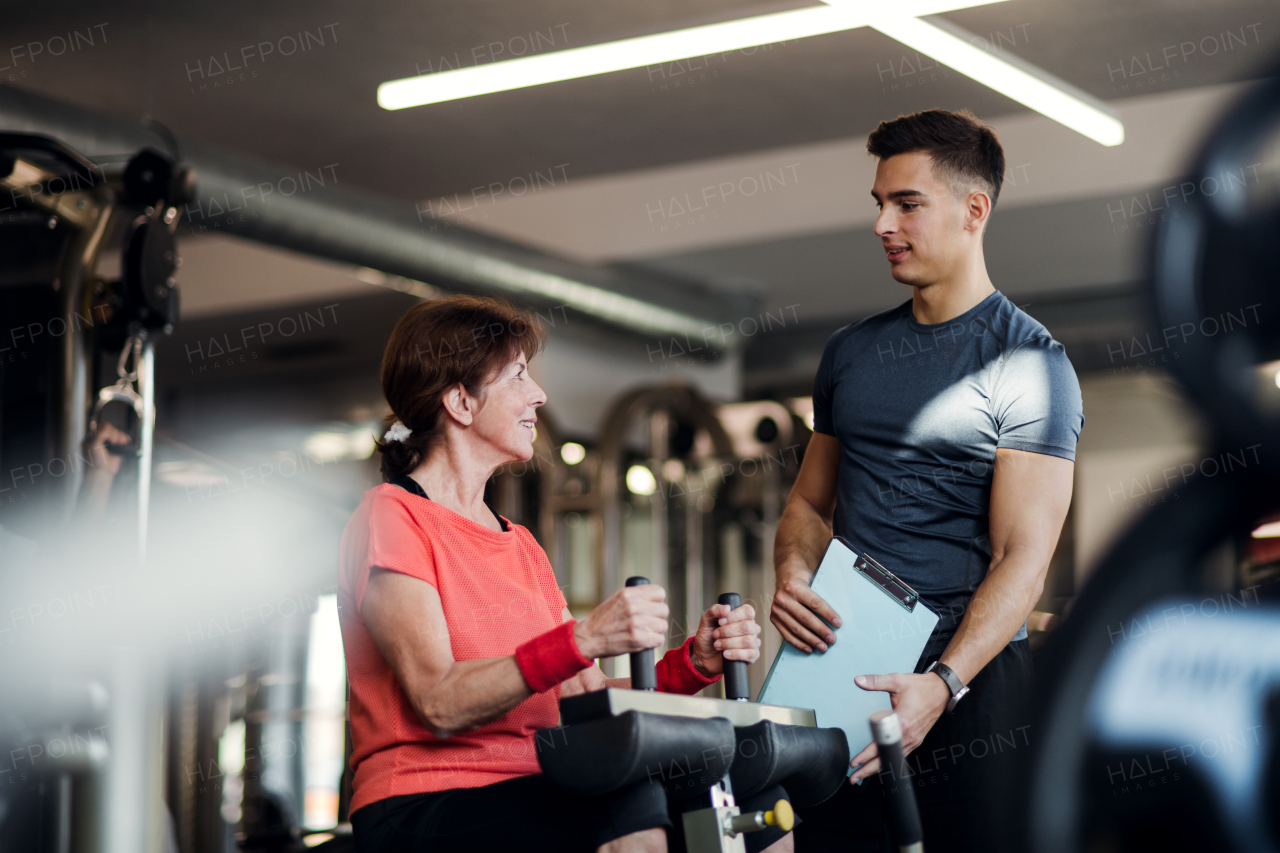 A cheerful female senior with a young trainer doing strength workout exercise in gym.