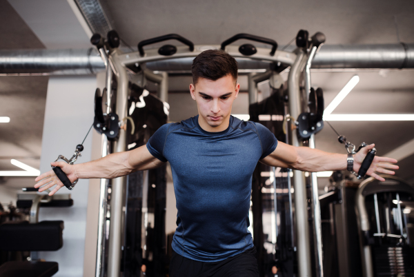 A concentrated young handsome man doing strength workout exercise in gym.