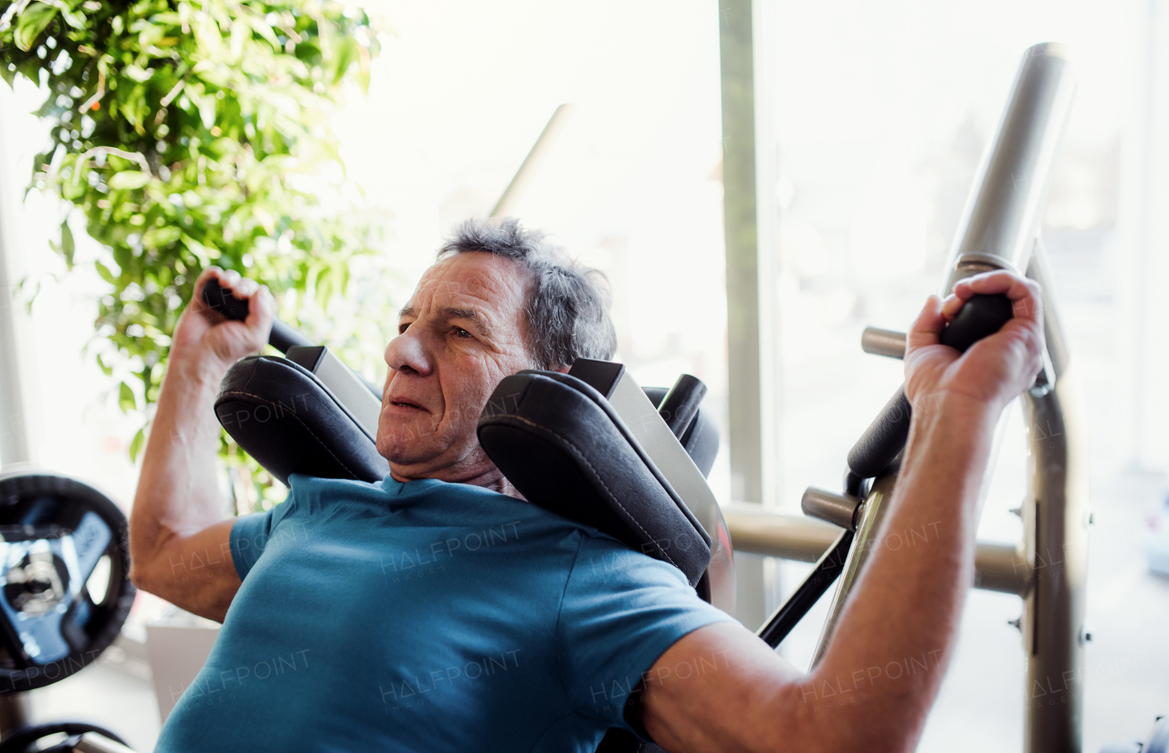 A concentrated senior man doing strength workout exercise in gym.