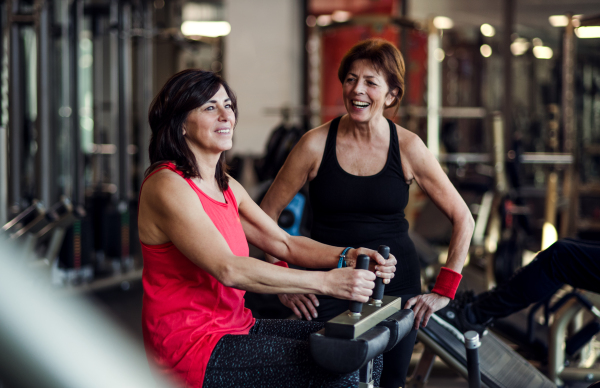 Two cheerful senior women friends in gym doing strength workout exercise.