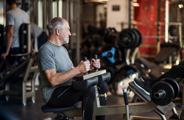 A senior man doing strength workout exercise in gym. A copy space.