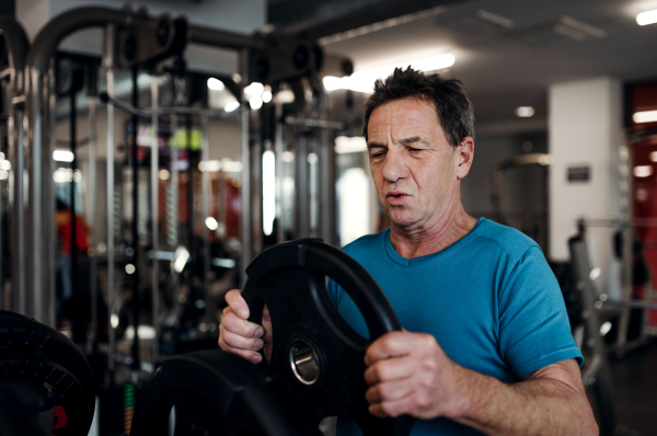 A senior man doing strength workout exercise in gym. A copy space.