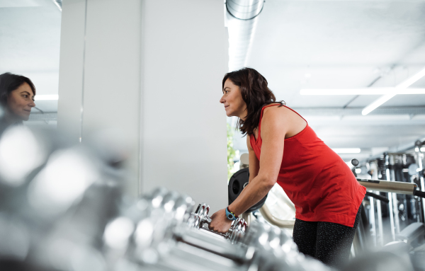 A happy female senior in gym doing exercise with dumbbells. Copy space.