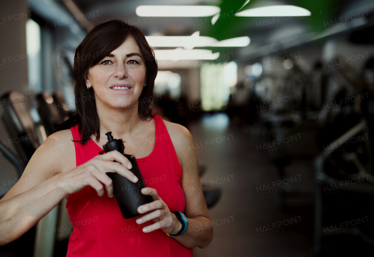 A content senior woman with water bottle in gym resting after doing exercise. Copy space.