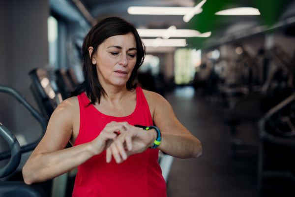 A content senior woman with smartwatch in gym resting after doing exercise, checking time. Copy space.